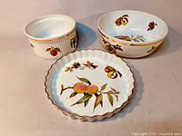 Image showing three Royal Worcester Evesham porcelain serving pieces: fluted tart dish, deep bowl, and ribbed casserole dish with fruit motifs and gold trim.