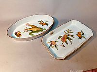 Two Royal Worcester Evesham porcelain serving dishes: one oval with corn and fruit design, one rectangular with peaches.
