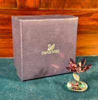 Swarovski crystal flower figurine next to original Swarovski box on green cloth background