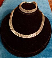 Front view of necklace and bracelet displayed on a black mannequin bust on blue cloth, showing full length and design details.