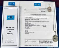 Appraisal certificate laid flat with pendant necklace draped across showing front detail of pendant and chain.