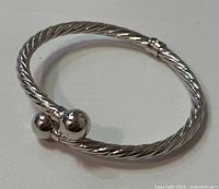 Side and angle view of open cable cuff bangle showing twisted cable design and polished ball end caps.