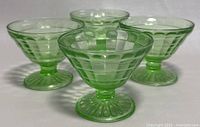 Four vintage green uranium glass sherbet bowls arranged in a group showing their shape, pattern, and color under daylight.