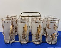 Frontal view of eight vintage drinking glasses with gold leaf designs in a metal caddy.