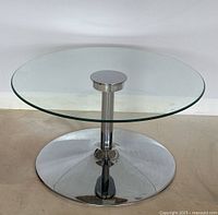 Full view of the round glass top coffee table on chrome base, showing clean clear top and reflective base.