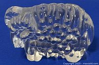 Clear art glass ram paperweight displayed on blue background showing full side profile, highlighting textured wool and curled detailed horns.