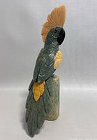 Front-right view of the green and yellow hand carved parrot figurine on stand showing detailed feathers and orange crest.