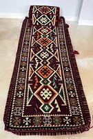 Full view of the toshak mattress cover rolled flat with the matching pillow placed at one end, showing geometric and tribal patterns in warm colors on a burgundy ground.