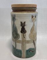 Front view of the pottery canister featuring three cats sitting on a wooden fence, with natural wood lid on top.