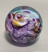 Top view of the spherical glass paperweight showing purple and yellow swirls with bubbles inside.
