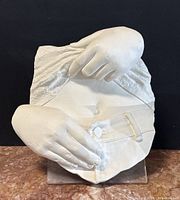 Front view of white sculpture showing hands lifting cloth revealing partial torso with navel and pants detail.