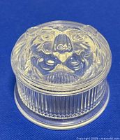 Clear crystal round trinket box with a sculpted lion head on the lid, set on a blue background.