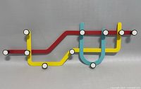 Full view of subway design metal coat rack with red, yellow, and blue lines and ten white-topped hooks.