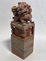 Front angled view of one Foo Dog seal showing carved details, natural jasper stone base, and hollow lattice section beneath the figure.