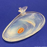 Opalescent glass oyster shell shaped dish with bird figurine on edge, showing its translucent blue milky color and swirled texture with the Sabino label on the base.