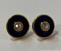 Front view of pair of round stud earrings with black onyx discs and clear center stones in 14K gold.