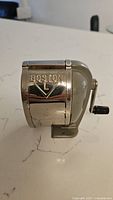 Side view of the vintage Boston-brand pencil sharpener with metal body and crank handle.