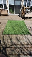 Full view of green artificial turf mat laid flat on wooden deck showing size and condition.
