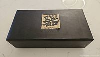 Closed black rectangular box with Japanese characters on label, containing the tea set.