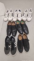 All seven pairs of men's shoes arranged in rows including white Adidas sneakers, black Zara sneakers, and black Clarks dress shoes.