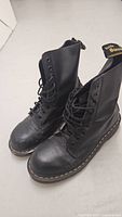Pair of black leather 10-eye Dr. Martens boots shown at slight angle, black laces and yellow stitching around sole visible.