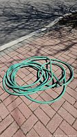 Coiled green garden hose on brick patio surface.