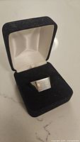 Man's ring with square flat top displayed inside open black velvet ring box with cream lining.