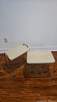 Two vintage MCM stools stacked and side by side on wood floor against white wall, showing overall shape, color, and dimensions.