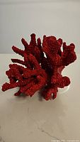Close-up image showing detailed texture and branching of the red imitation coral piece on a white surface.