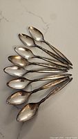 Set of eight silver spoons arranged on a marble surface, showing their overall condition and size.