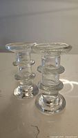 Pair of clear glass candlestick holders with two rings midsection, shown side-by-side on a neutral background.