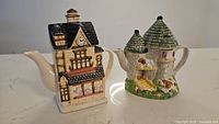 Photo of two whimsical ceramic teapots shaped like buildings, placed side by side on a white surface