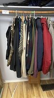Hanging men's clothing including jackets, sweaters, shirts, and vests in a closet, showing fabric colors and patterns