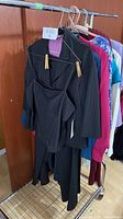 Photo showing a black pinstripe women's blazer jacket with matching skirt or pants on a clothing rack alongside other colorful clothing items.
