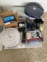 Overview photo showing two iRobot Roomba robotic vacuum cleaners, boxed answering machines, boxed radio cassette recorder, Durabrand hair dryer box, flashlight, and assorted cords.