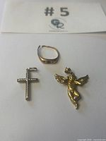 Three pieces laid flat: ring, cross pendant, cherub pendant