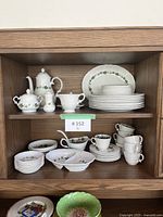 Full view of shelving unit with multiple pieces of white ironstone china with a green leaf pattern including teapot, cups, plates, and bowls.