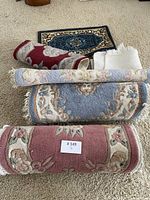 Six small area rugs rolled and laid out on carpeted floor, showing colors, patterns, and fringes.