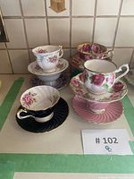 Seven vintage bone china tea cups and saucers with floral patterns and assorted pastel and black colors arranged on a table.