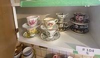 Photo showing 4 sets of tea cups and saucers with assorted floral patterns on kitchen cupboard shelf.