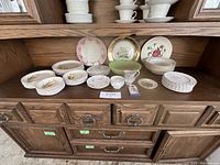 Wide shot of the china set displayed on a wooden hutch showing plates, bowls, and stacked cups