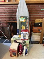 Wide shot showing all items in the lot, including ironing board, boxed appliances, two irons, and other small household items.