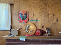 Shelf display of Indigenous art and wood carvings including hand drum, round plaque, wooden masks, and animal carvings.