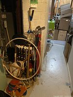 Overall view of the sports equipment pile in a narrow hallway showing hula hoops, golf clubs, croquet mallets, badminton rackets, and sporting bags