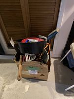 Full view of the cardboard box with assorted vehicle supplies and tools including funnels, hammer, hoses, and brush inside and around the box.