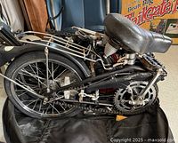 Side close-up showing folded bike frame, metal rear rack, bicycle chain system, and seat.