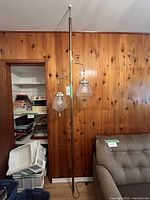 Full view of brass-finish telescoping rod with two hanging glass shades installed between floor and ceiling against wood-paneled wall