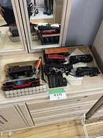 Photo showing multiple vintage model train cars including caboose, locomotive, and freight cars on top of a wooden dresser.