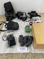 Overall view of five cameras, binoculars, radio and wooden microscope case arranged on white surface