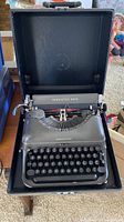 Front view of vintage Remington Rand typewriter inside its black carrying case, showing keyboard and paper holder.
